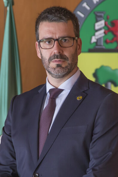 Foto oficial tipo retrato de José María Carvajal González delante de una pared con la bandera y el logo de la universidad.