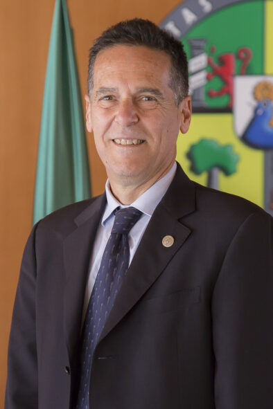 Foto oficial tipo retrato de Agustín García García delante de una pared con la bandera y el logo de la universidad.