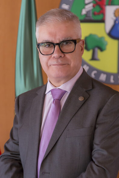 Foto oficial tipo retrato de Pedro Fernández Salguero delante de una pared con la bandera y el logo de la universidad.